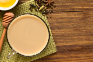 Homemade Indian Masala Chai Tea made of black tea, a variety of spices and mixed with milk, honey and ingredients on the side, photographed overhead on dark wood with natural light (Selective Focus, Focus on the top of the tea)